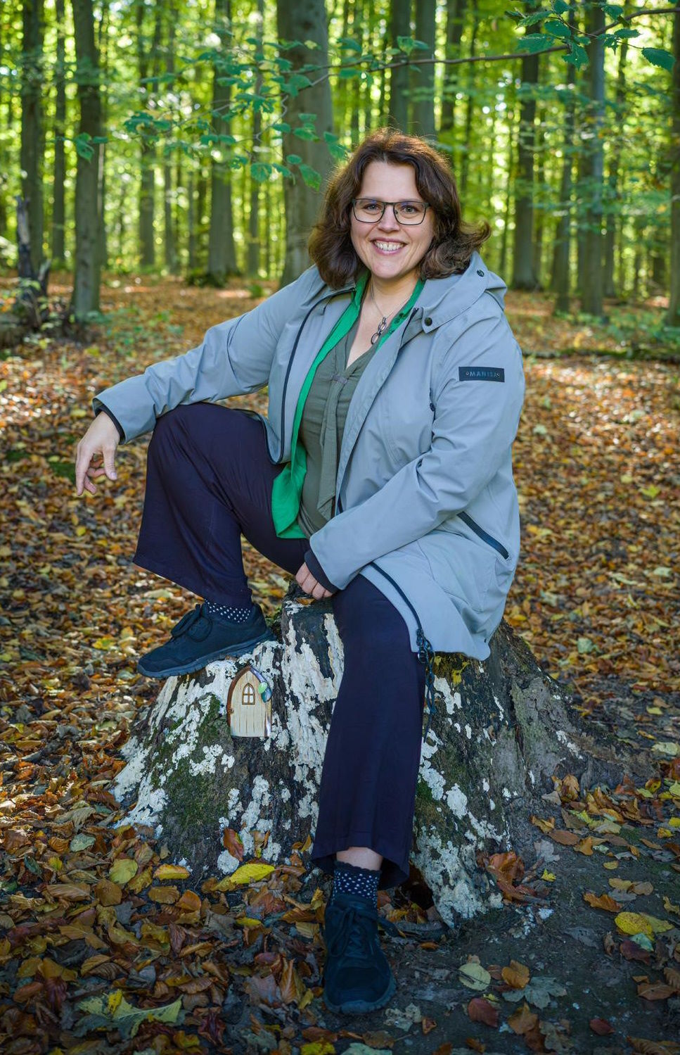 Kinderbuchautorin Jana Haverbier auf einem Baumstumpf im Wald mit handgefertigter Zaubertür.
