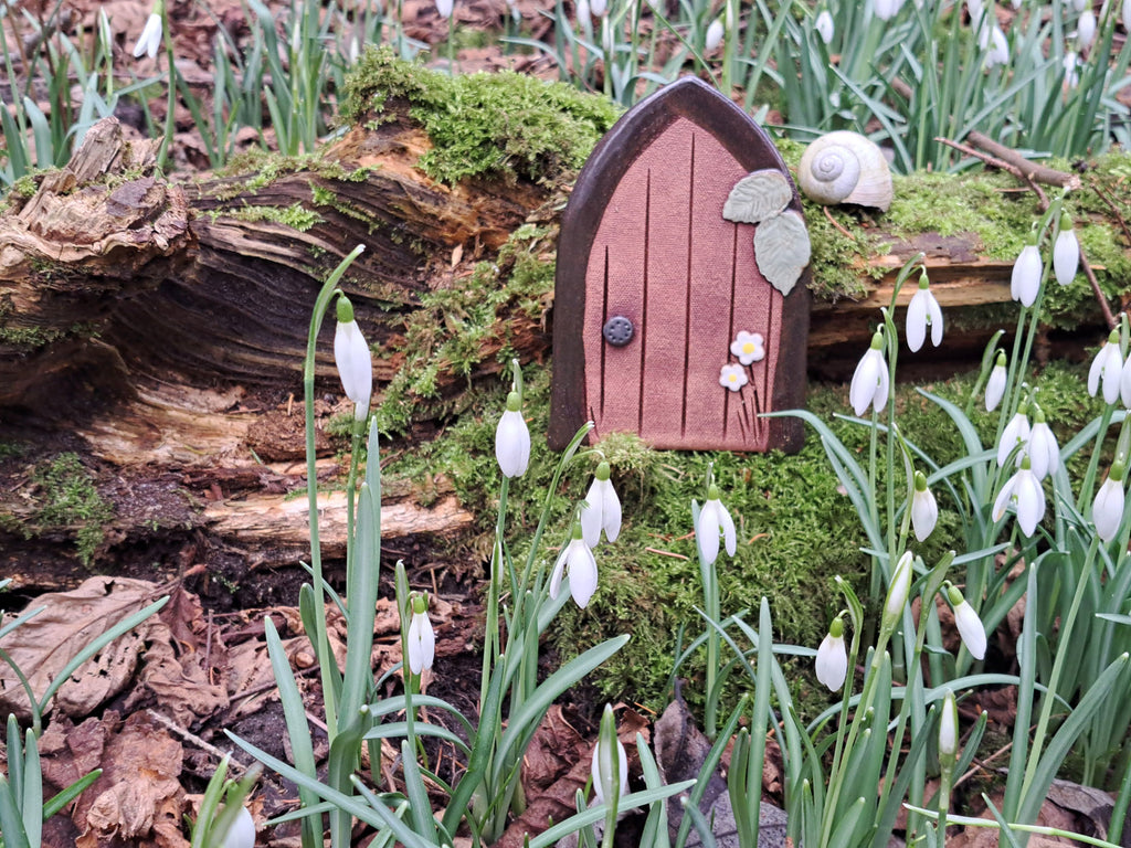 Eine handgefertigte Zaubertür aus Ton steht im Wald mit Schneeglöckchen passend zum Kinderbuch Der kleine Zauberer Pfifferling.