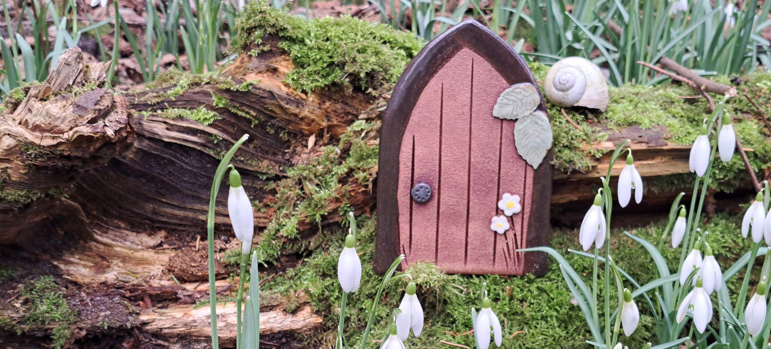 Eine handgefertigte Zaubertür aus Ton steht im Wald mit Schneeglöckchen passend zum Kinderbuch Der kleine Zauberer Pfifferling.
