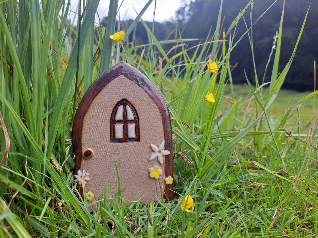 Eine handgefertigte Zaubertür aus Ton zum Kinderbuch Der kleine Zauberer Pfifferling steht auf einer Wiese mit Blumen.